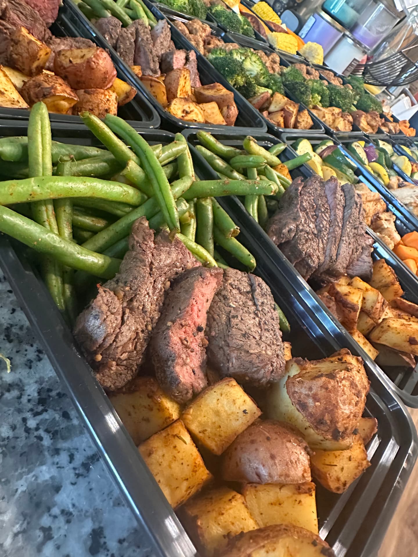 Trays of freshly prepared steak, potatoes and vegetables on a meal prep line
