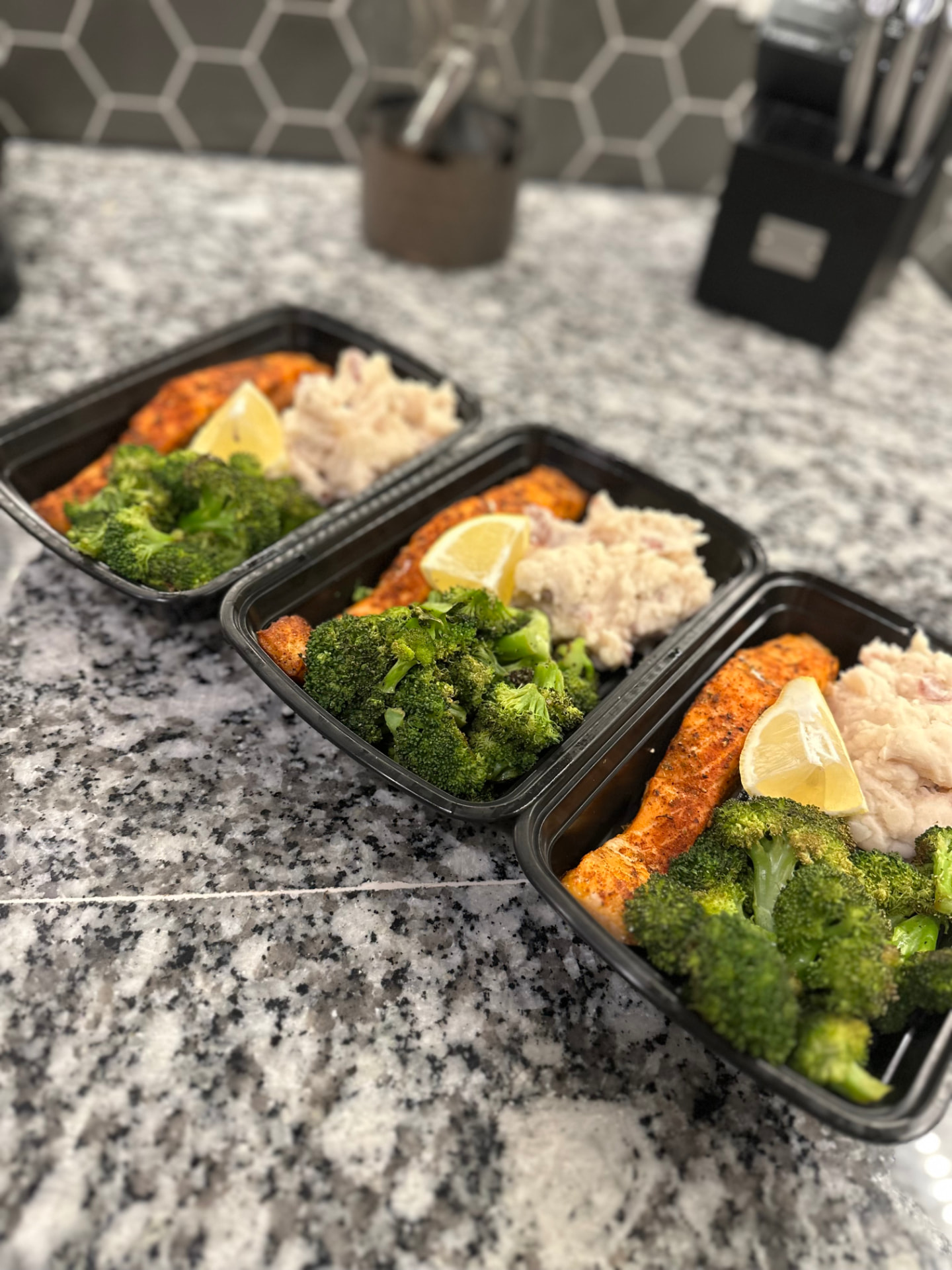 Prepared salmon, broccoli, and mashed potato meals on a kitchen counter