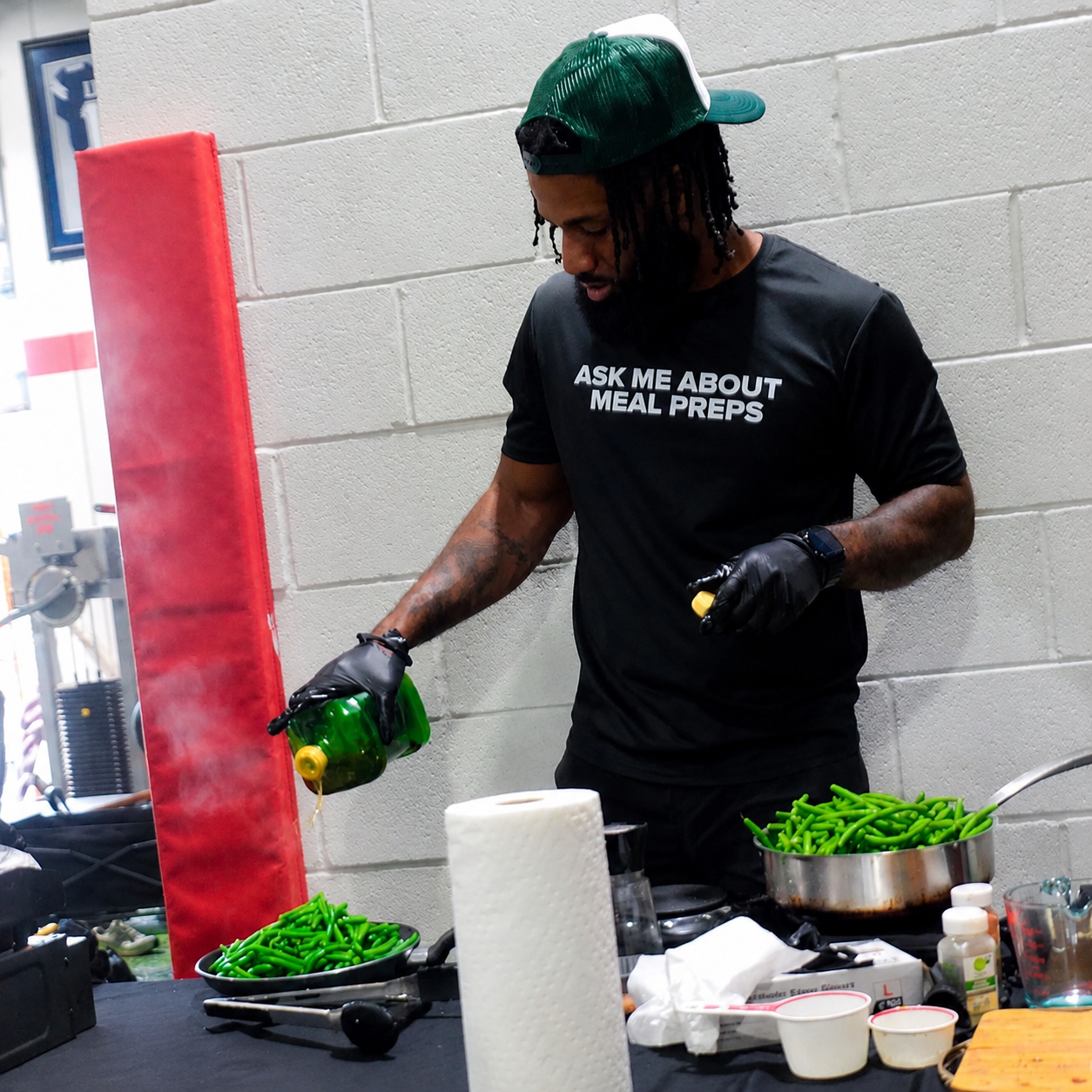 Chef in an E's Healthy Eats cap preparing green beans at a gym demo